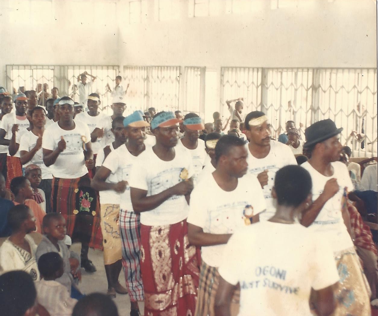 A group of people in white T-shirts, blue visors, and colorful skirts march in protest.