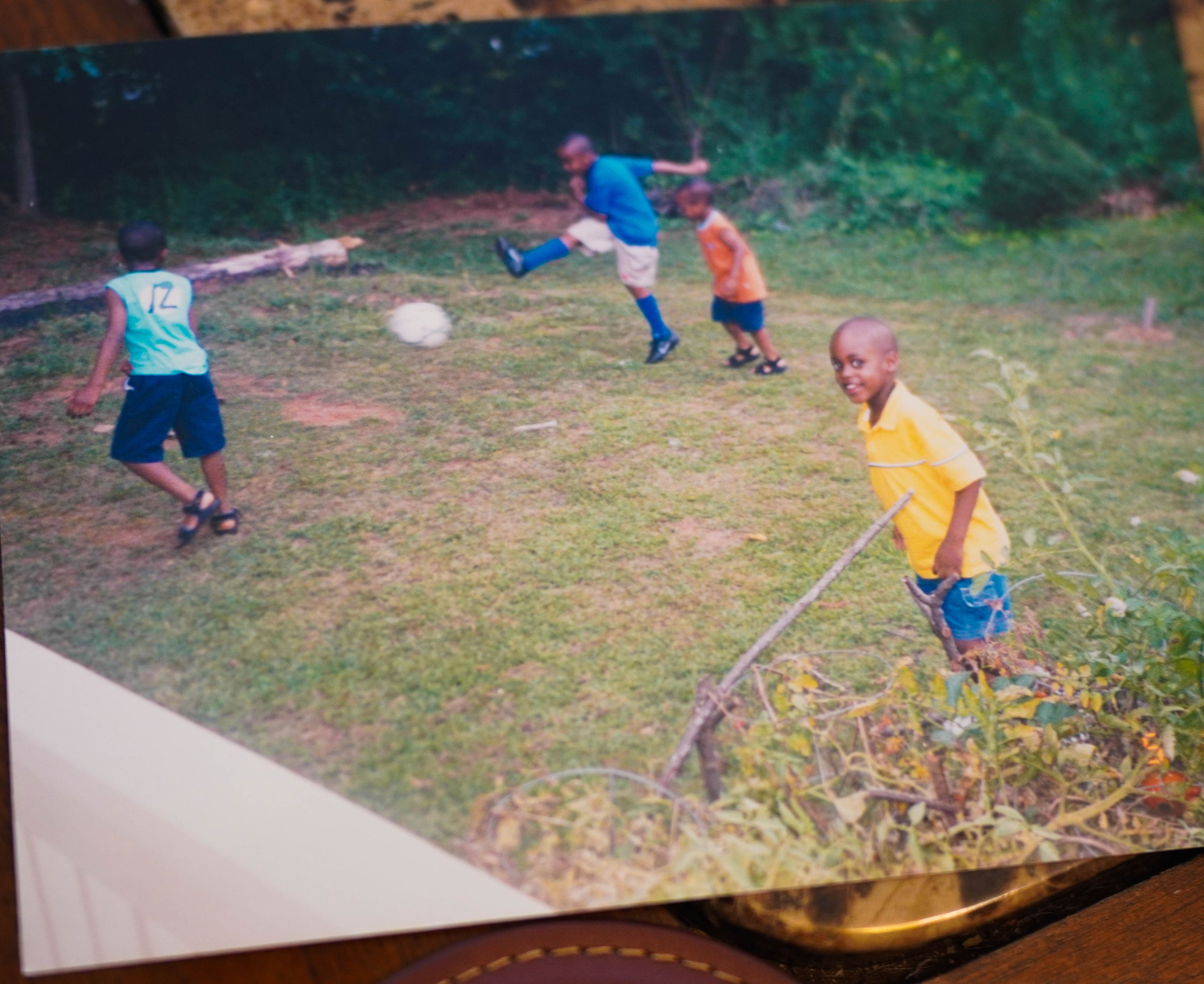 A picture of boys playing soccer while another boy works in the garden