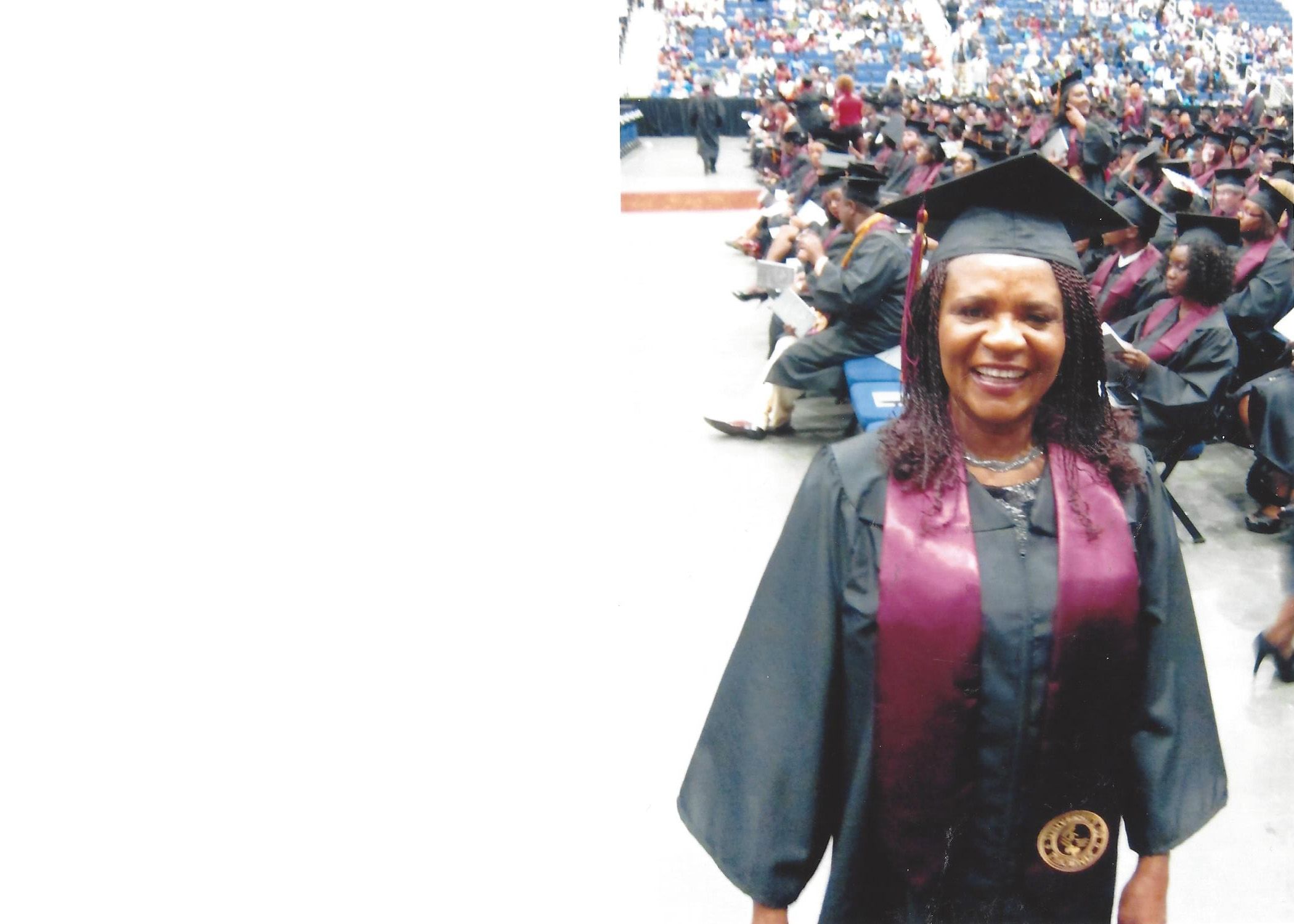 A person at a graduation ceremony wearing a black cap and gown and a burgundy stole.