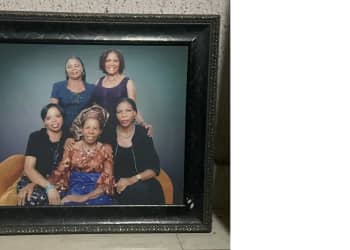 A framed picture of five women, three sitting and one standing.