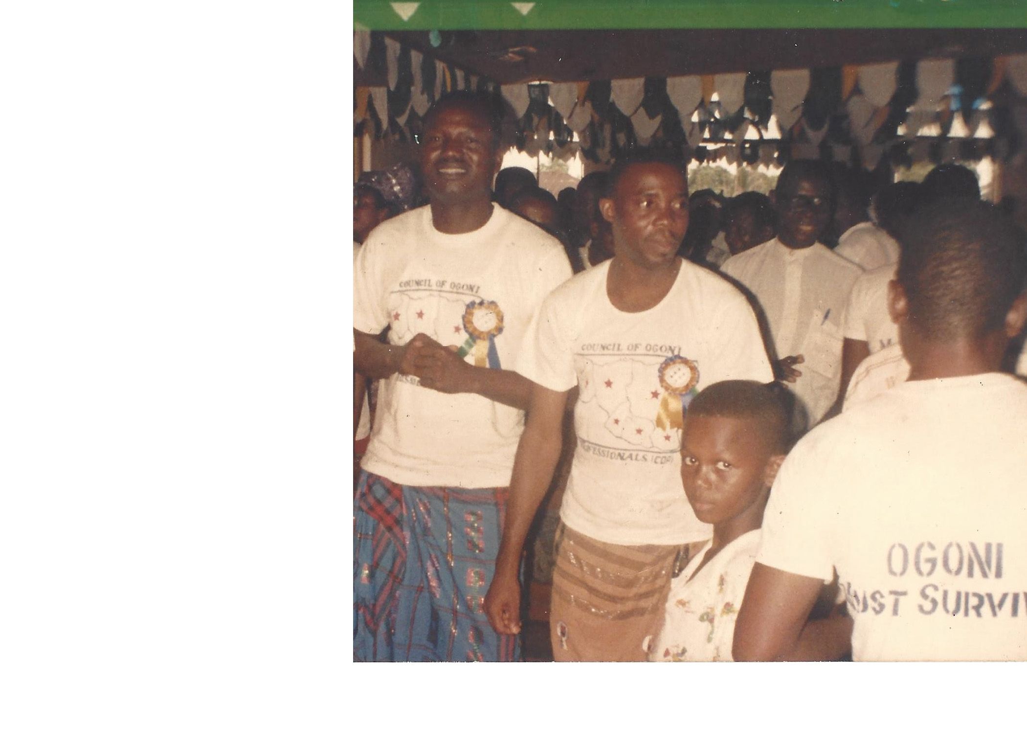 People wearing white T-shirts, one turned around with the words "Ogoni Just Survive"