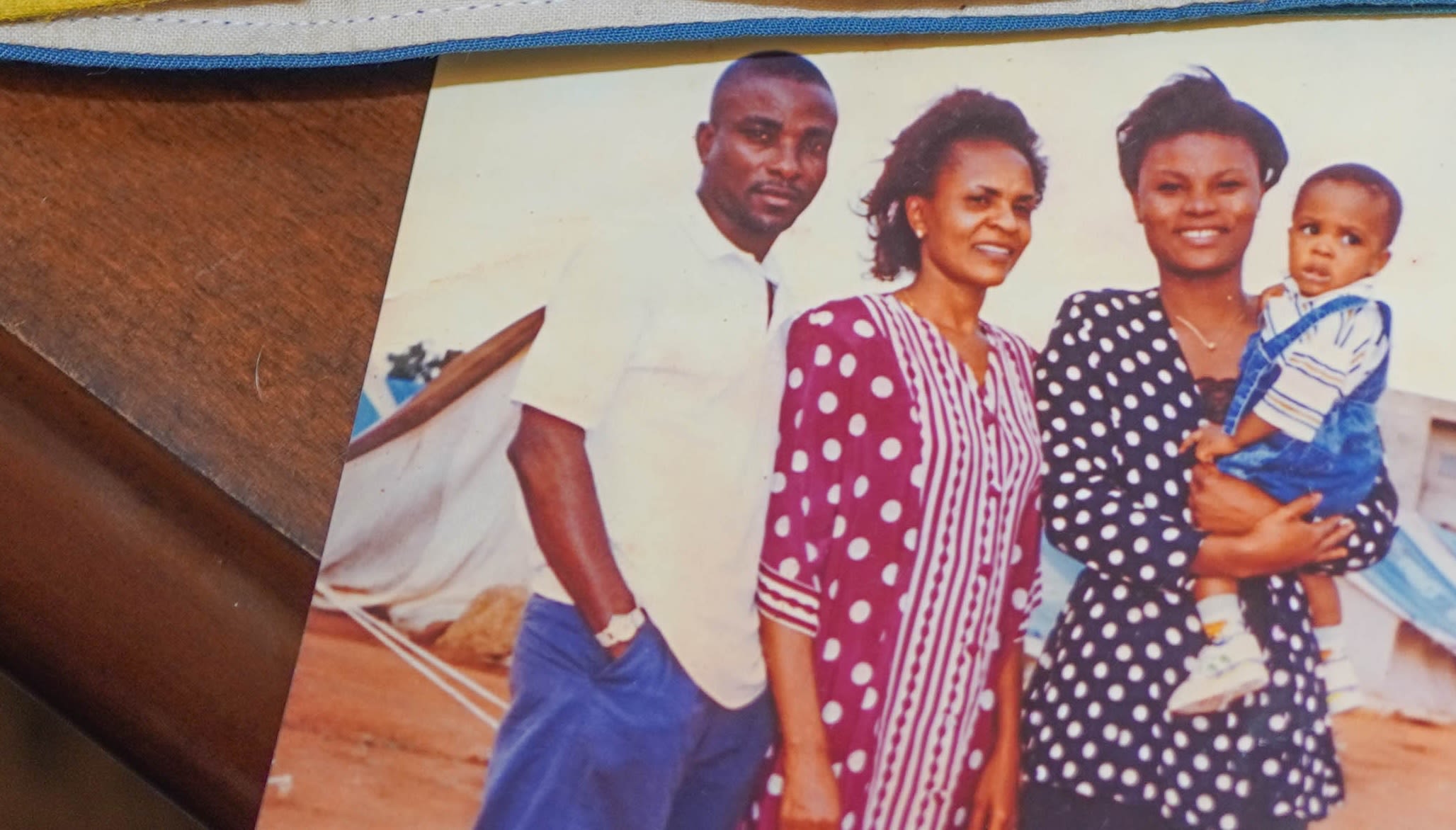 A picture of three adults, one holding a baby, standing in front of refugee tents.