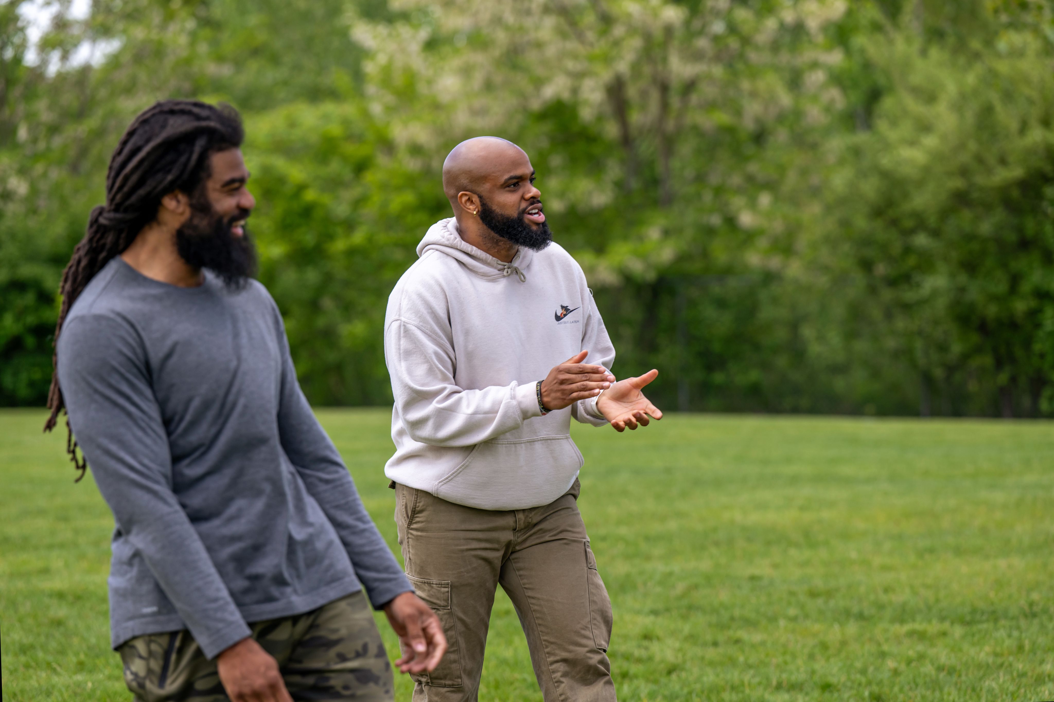 One man with a fluffy beard and long dreadlocks laughs while another man who's bald with a beard claps.